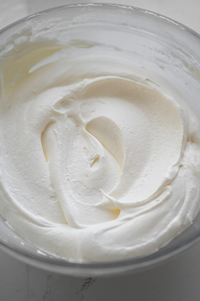 A creamy pudding and whipped topping frosting in a large clear bowl.