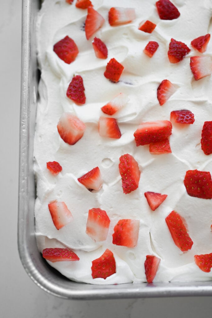 A cake topped with a white frosting and diced fresh strawberries.