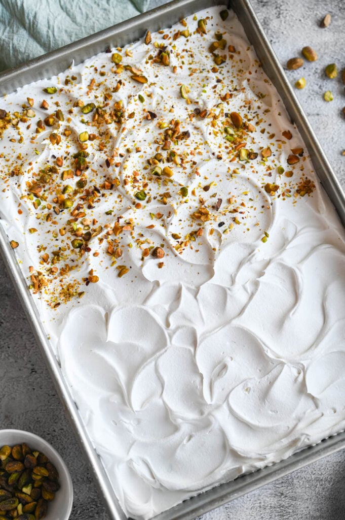 A 9x13-inch cake topped with whipped cream and pistachios on half of it.