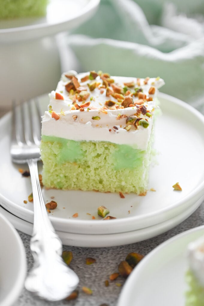 A square piece of pistachio poke cake on a white plate.