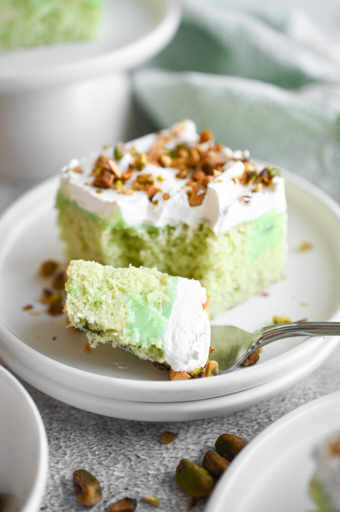A slice of pistachio poke cake with a fork grabbing a bite.
