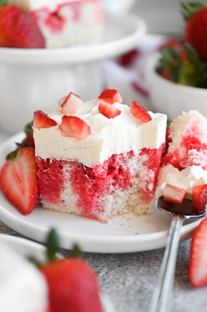 Strawberry Poke Cake with Real berries and a creamy frosting on a white plate.