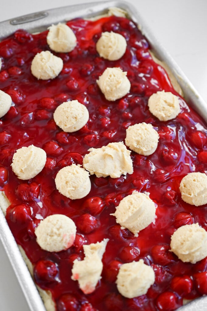 Dollops of batter on top of a jellyroll pan full of a cherry dessert.