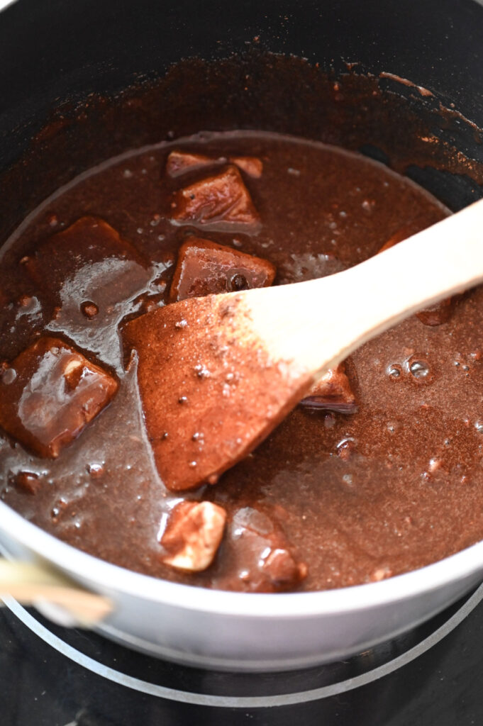A melty chocolate mixture in a saucepan with a wooden spoon.