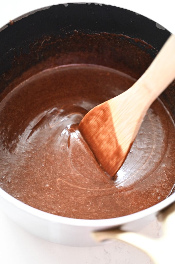 A wooden spoon stirring peanut butter into a chocolate mixture.