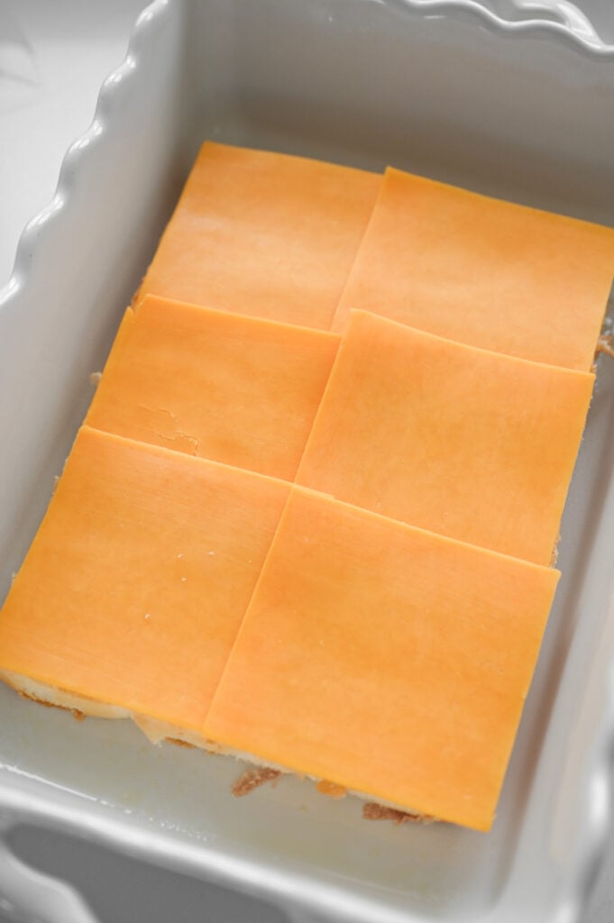 Cheddar cheese slices topping a sheet of buns in a pan.