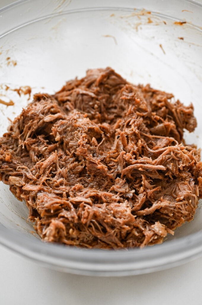 BBQ pulled pork mixed up in a clear glass mixing bowl.