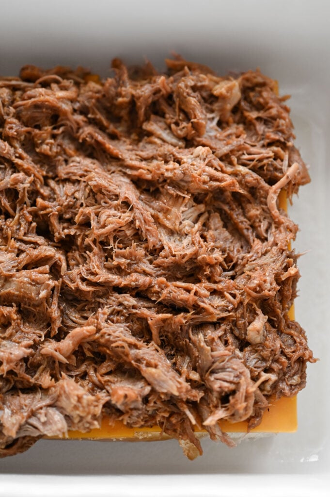 Cheese and bbq pulled pork layered on slider buns in a white dish.
