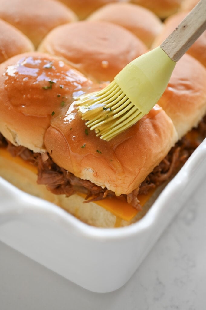 A light green brush spreading a buttery mixture over sliders.