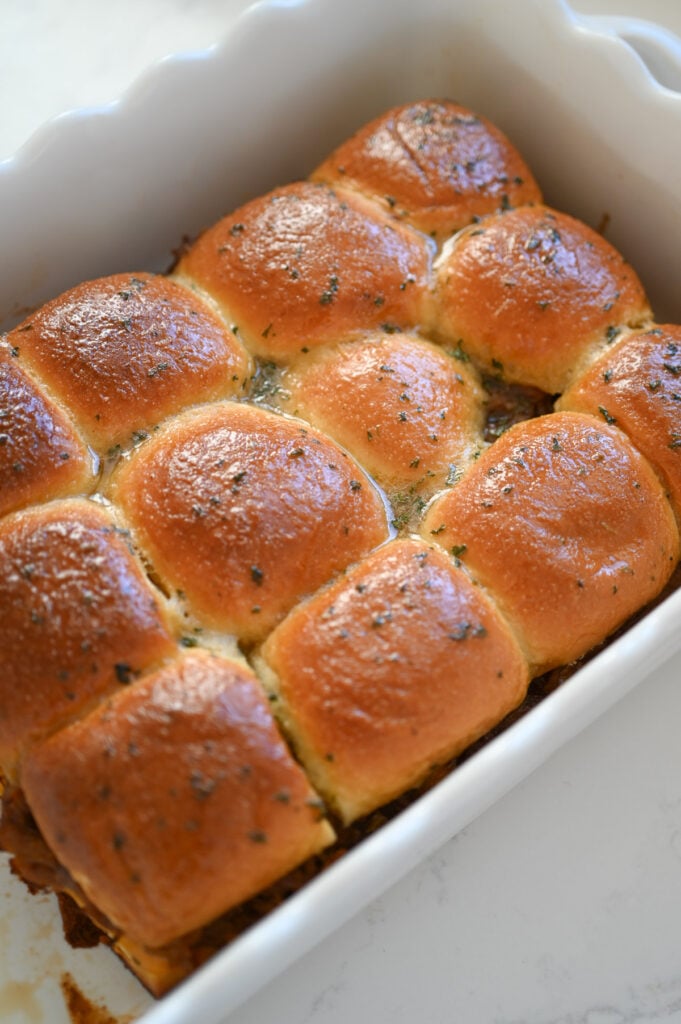 Baked sliders in a white ceramic dish.