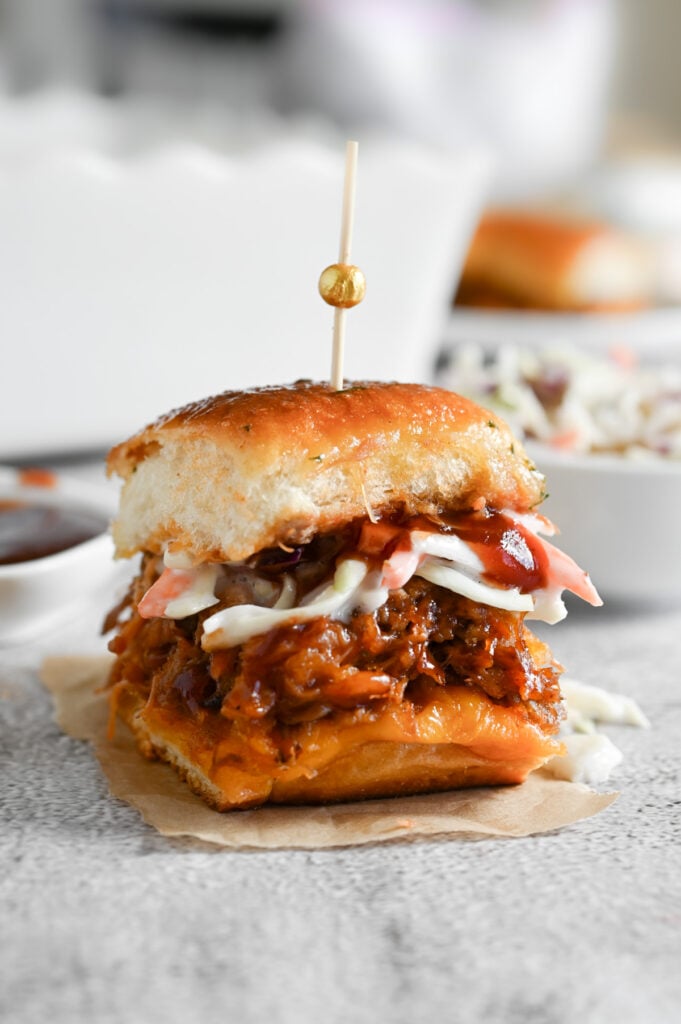 A pulled pork slider with coleslaw on top and held together with a toothpick.