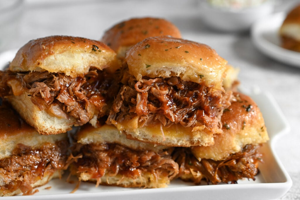 Several pulled pork sliders on a white serving tray.