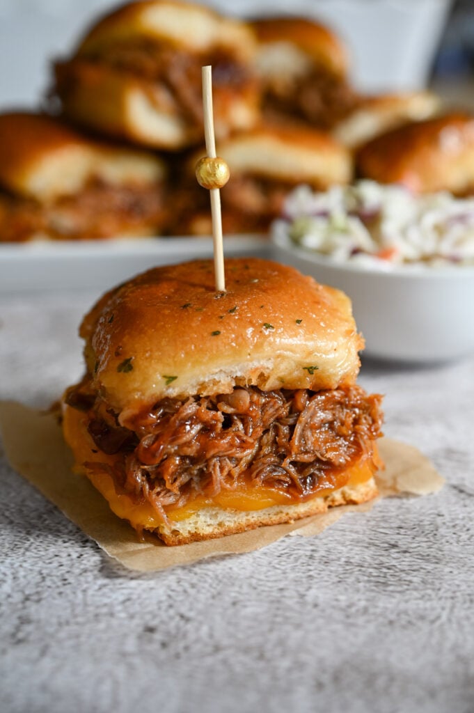 A pulled pork slider with cheese on a small piece of parchment paper.