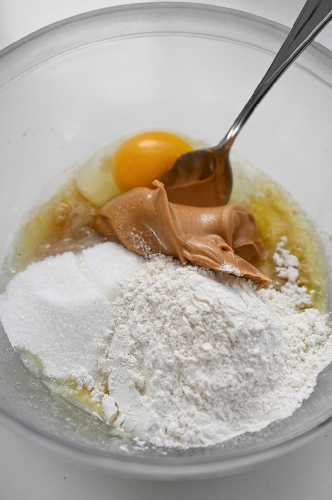 The ingredients for a peanut butter batter in a clear glass bowl.