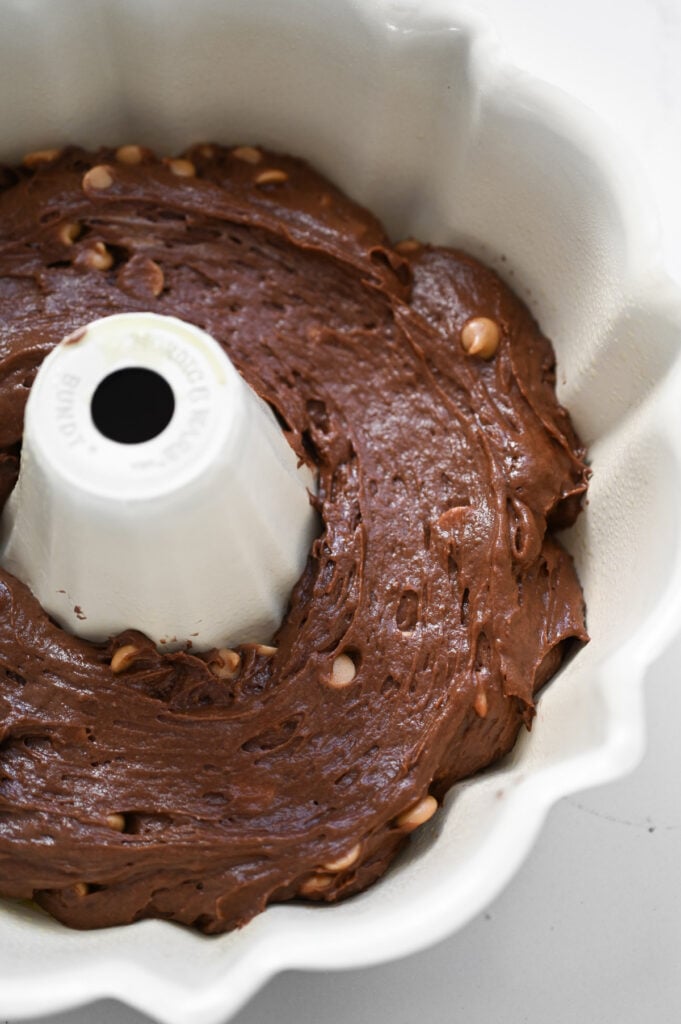 A chocolate cake batter with peanut butter chips spread into a bundt cake pan.