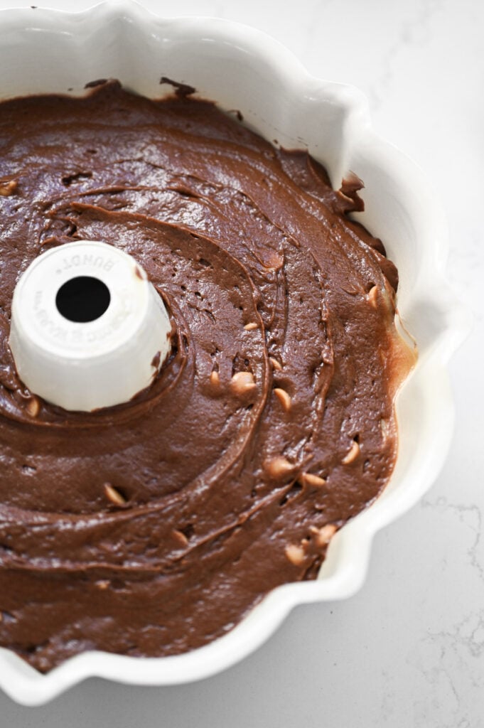 A chocolate batter with peanut butter chips spread into a white bundt cake pan.