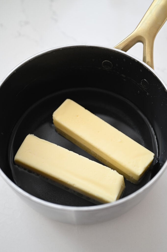 Two sticks of butter and some water in a saucepan.