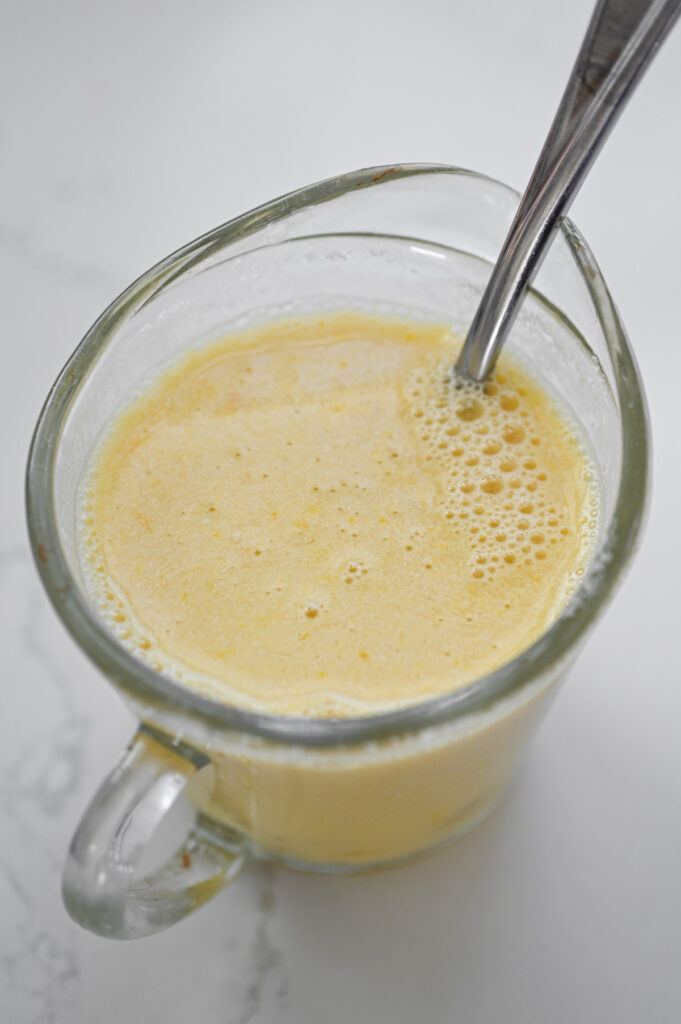Liquid ingredients for a cake stirred together in a small liquid measuring cup.
