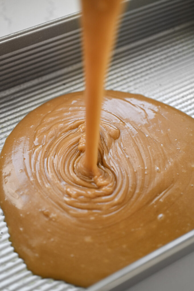 A glossy, smooth caramel-colored cake batter being poured into a greased pan.
