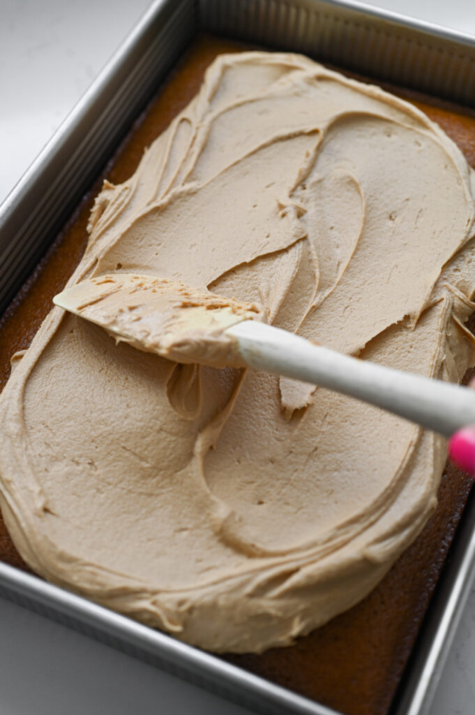 A spatula spreading frosting over a sheet cake.