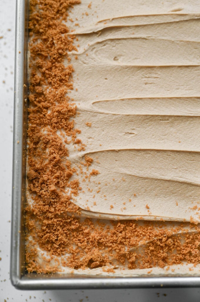 A cake with frosting and biscoff cookie crumbs around the edge of the cake.