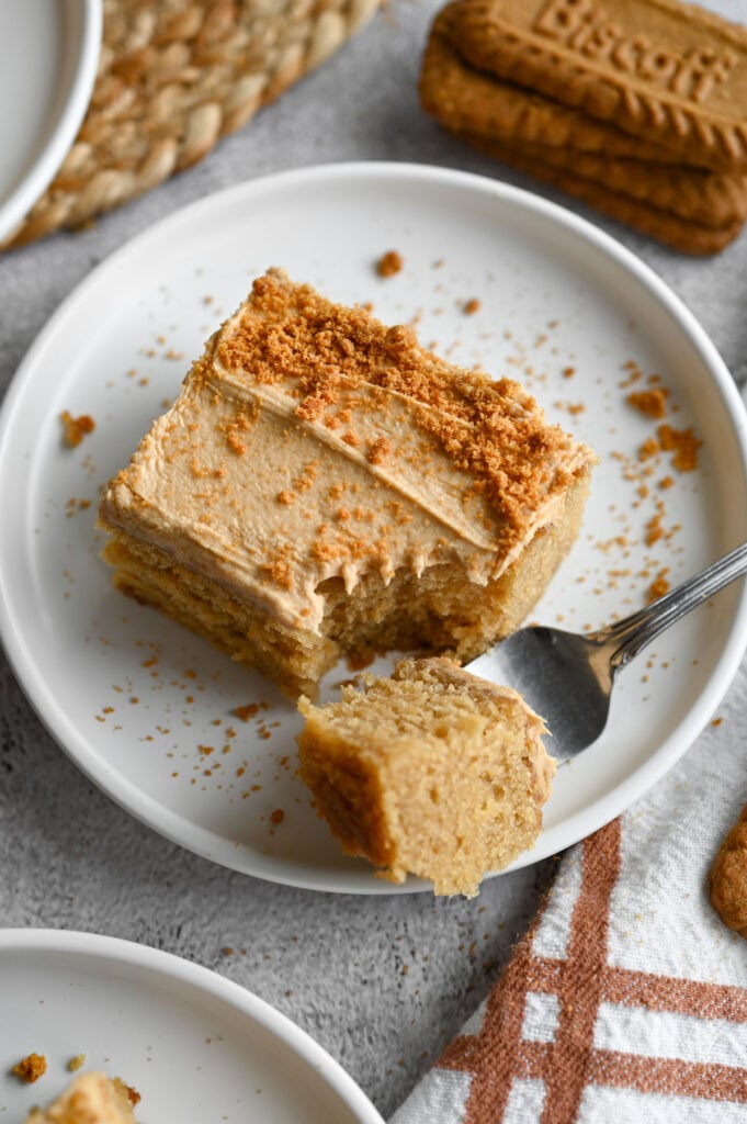 A piece of Biscoff sheet cake on a white plate with a bite out of it.