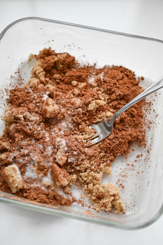A fork mixing sugars and cocoa powder in a deep dish square pan.