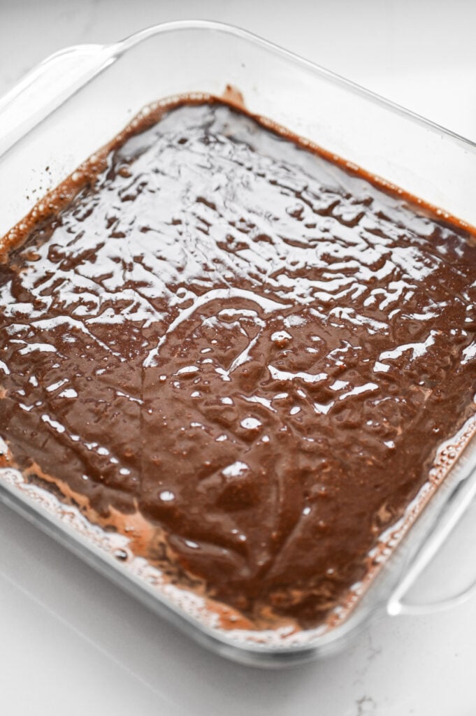 Brownie batter in a square clear glass baking dish.