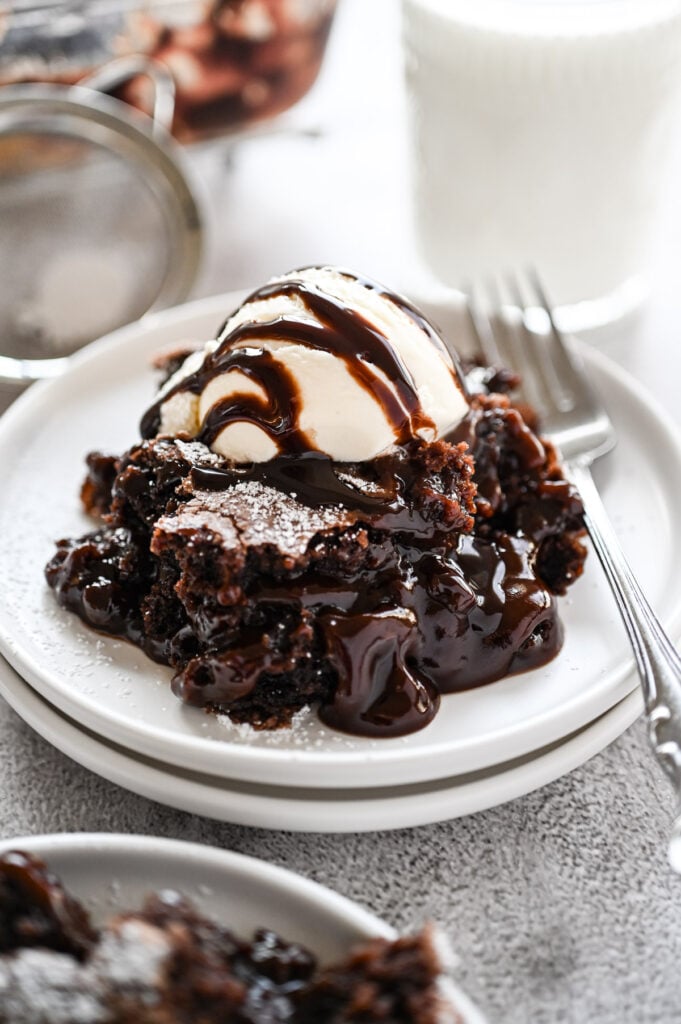 A spoonful of brownie cobbler on a plate with vanilla ice cream and a chocolate sauce.