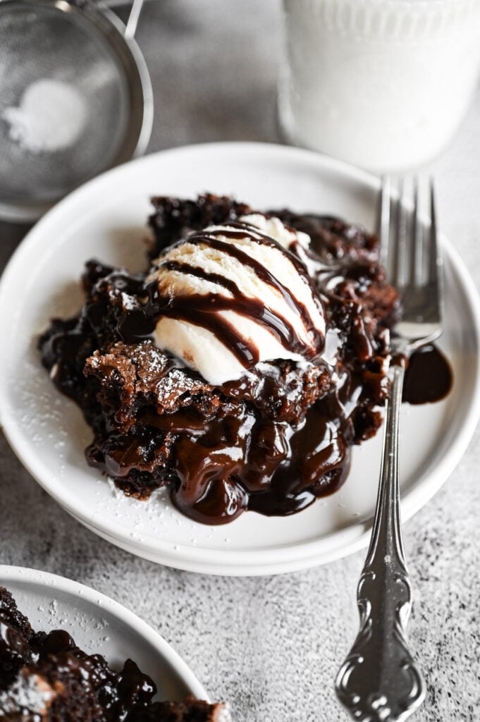A spoonful of brownie cobbler on a white plate with a fork next to it and a glass of milk on the side.