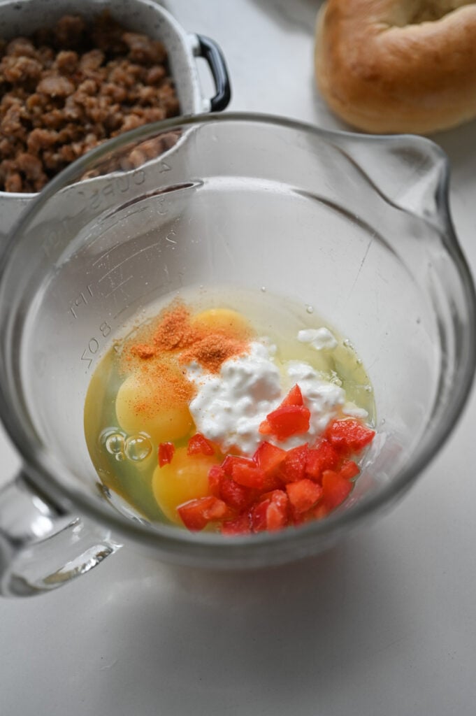 Eggs, seasoned salt, cottage cheese, and diced red peppers in a clear glass bowl.