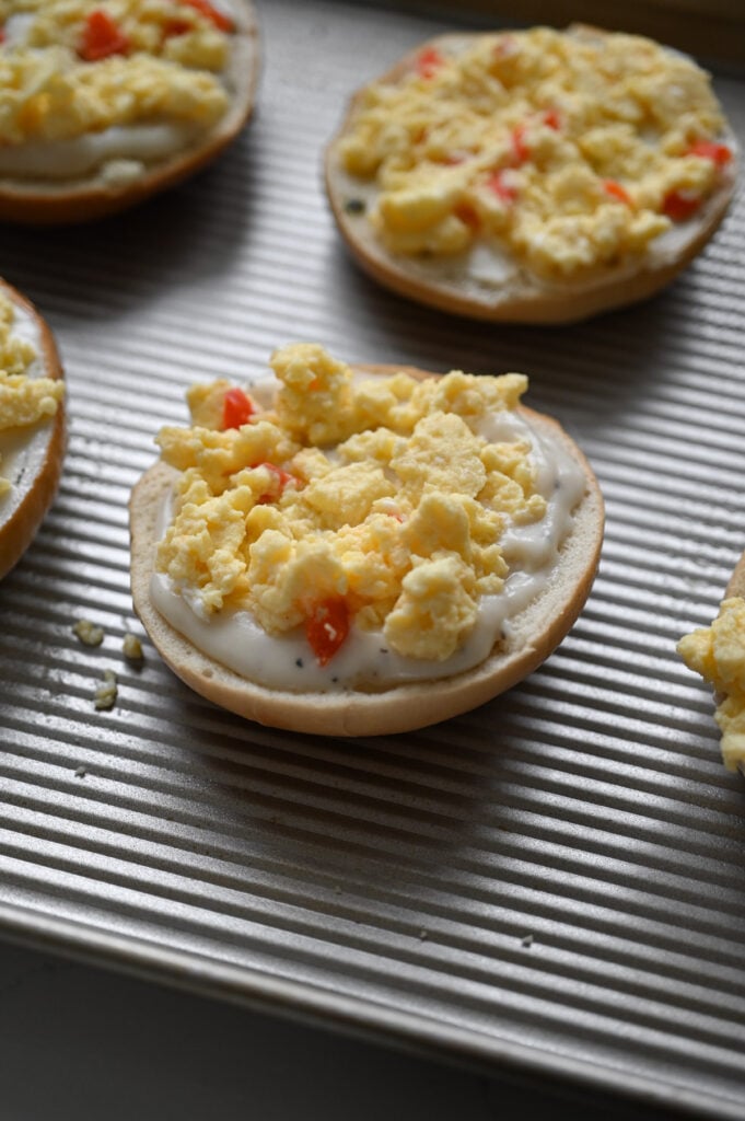 A bagel with white gravy and scrambled eggs on top.