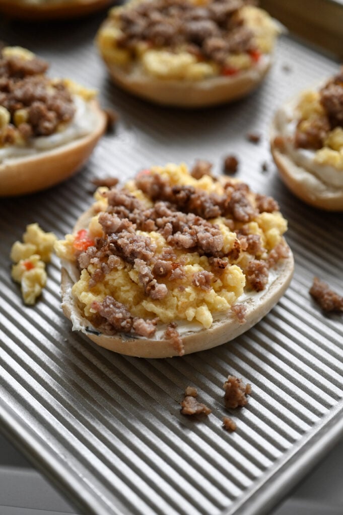 A bagel with cream cheese, scrambled eggs, and sausage layered on top.