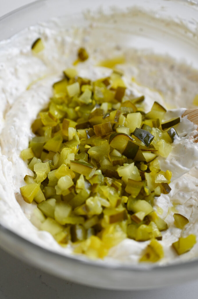 Diced pickles being stirred into a bowl of creamy dip.