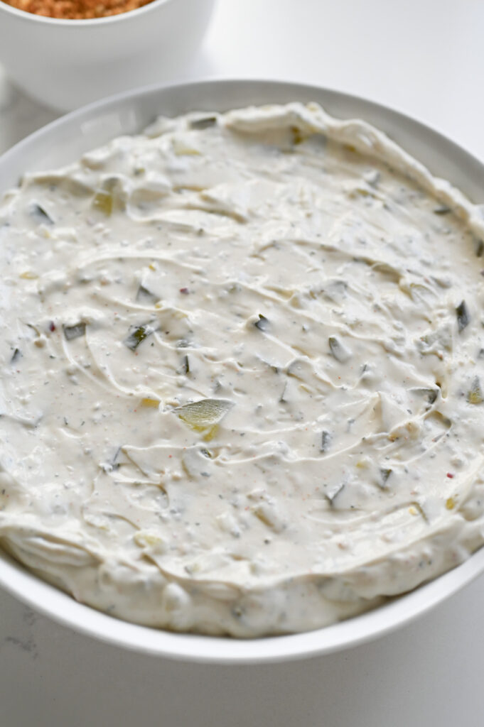 A pickle dip spread into the bottom of a shallow bowl.