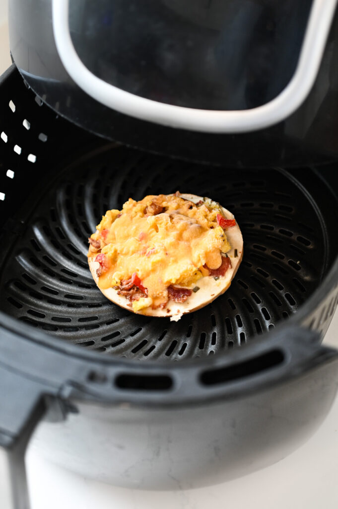 A frozen breakfast pizza bagel in the basket of a black air fryer.