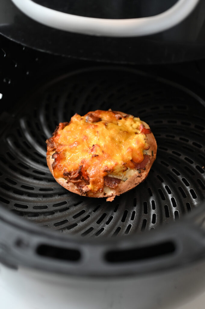 A cooked breakfast pizza bagel in the basket of a black air fryer.