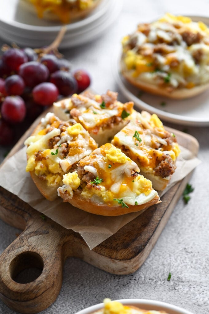 A bagel half topped with gravy, scrambled eggs, sausage and cheese cut into 4 "slices" on a wooden board.