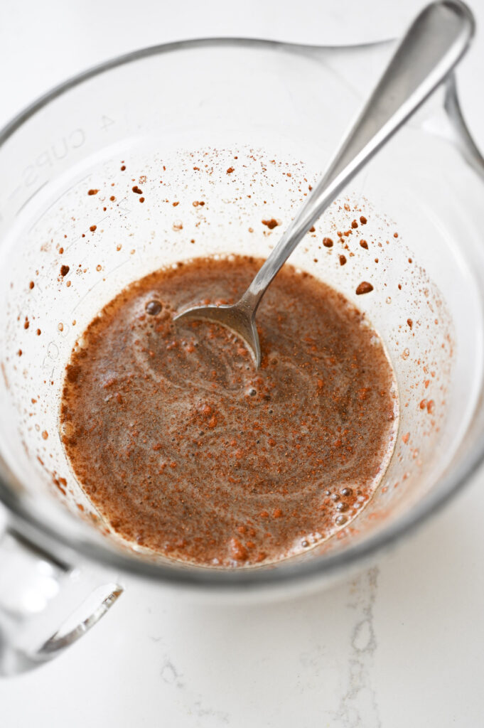 A brown liquid in a liquid measuring cup with a spoon.