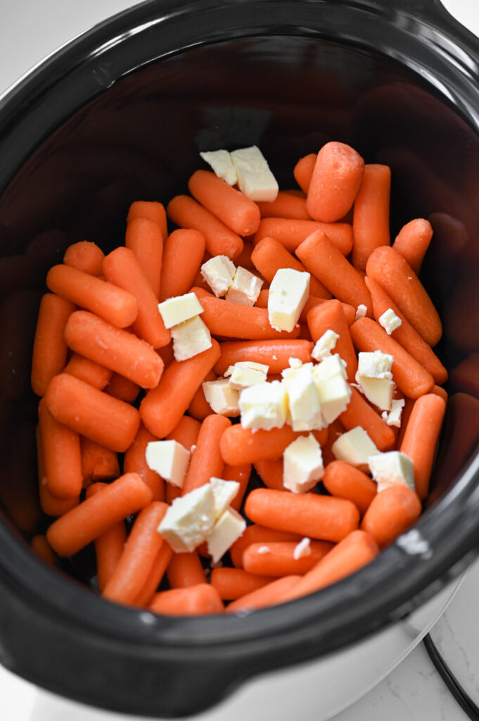 A black crock with baby carrots and cubed butter.