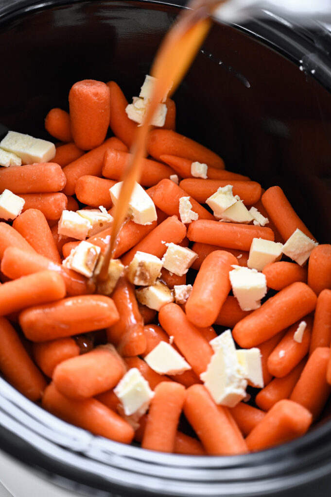 A brown sugar liquid being poured into a crockpot with carrots and butter.