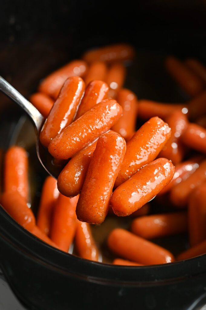 A spoonful of glazed baby carrots on a silver spoon.