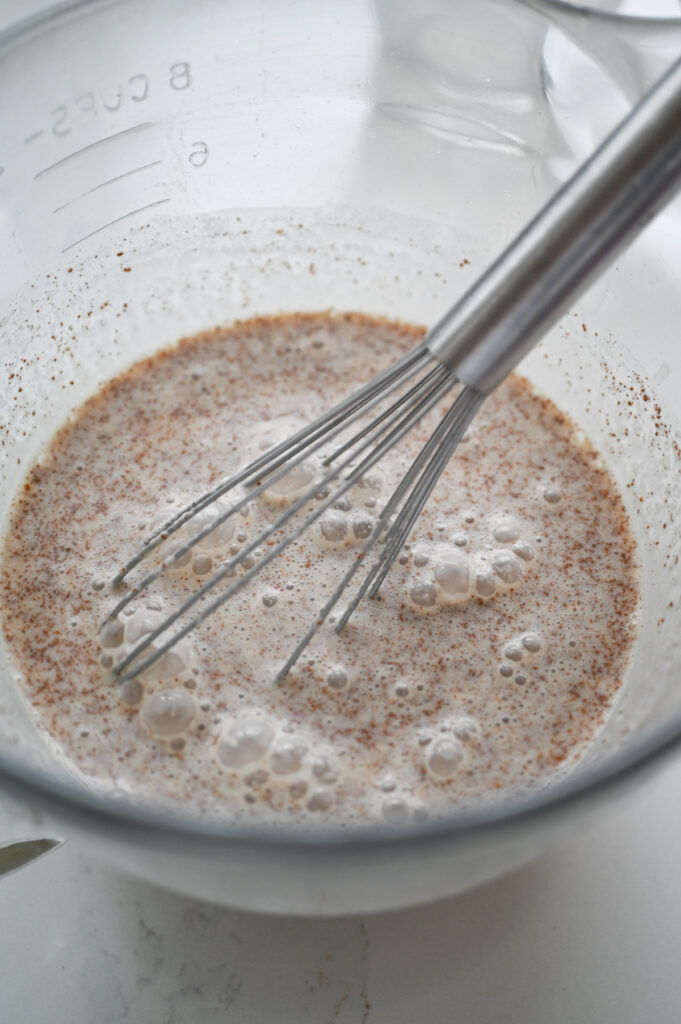 A whisk combining heavy cream, milk, cinnamon, brown sugar, maple syrup and vanilla.