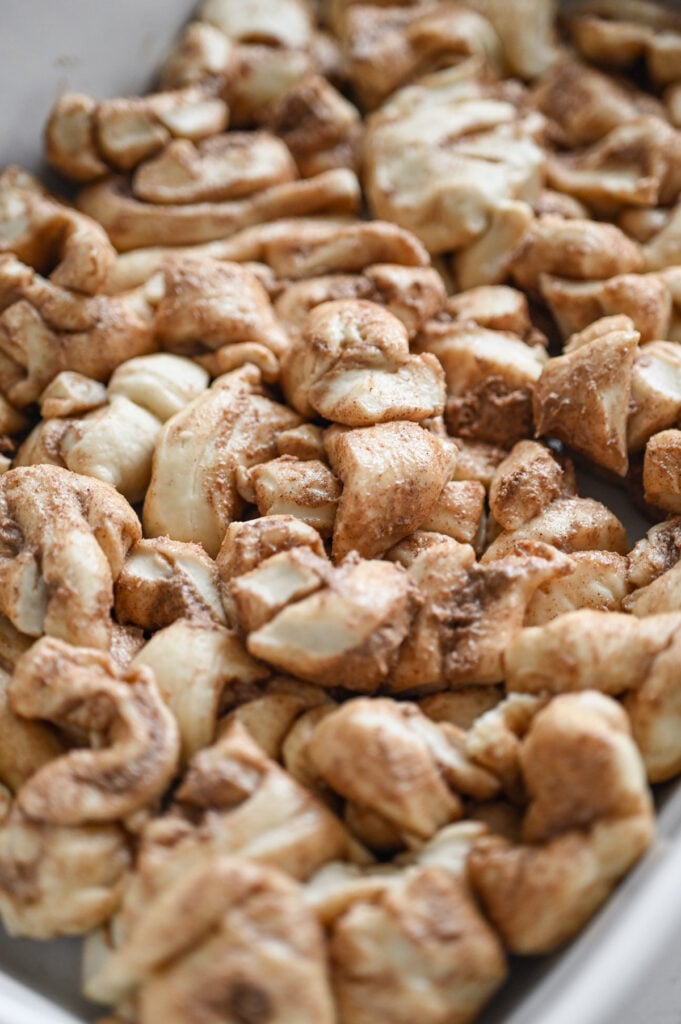 Cut up cinnamon rolls in the bottom of a white baking dish.