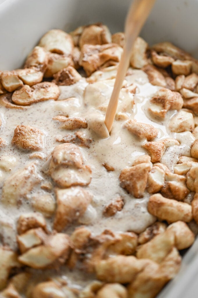 Pouring a custard over a pan of cut up cinnamon rolls.