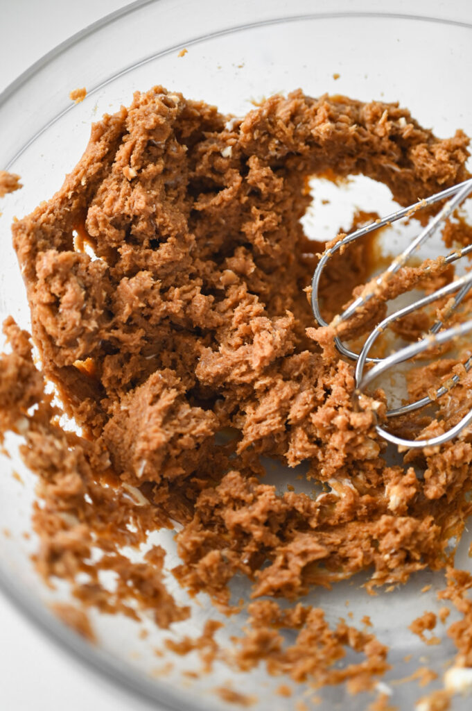 The beaters of an electric mixer in a bowl with cream cheese and Biscoff cookie butter.