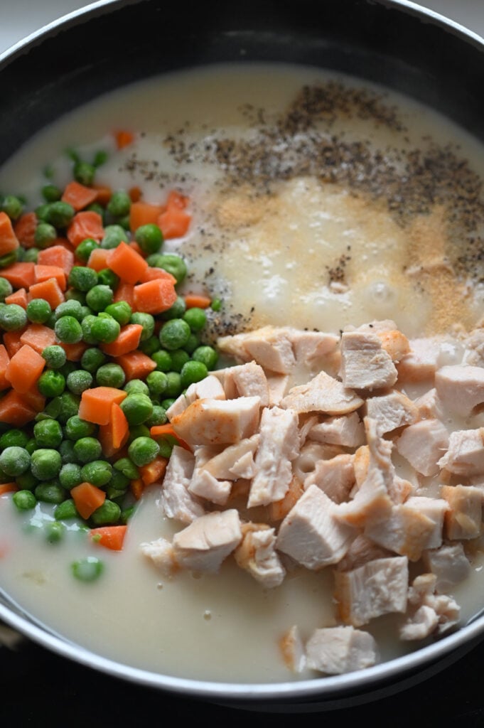 A sauce with chicken, vegetables and seasoning being added.