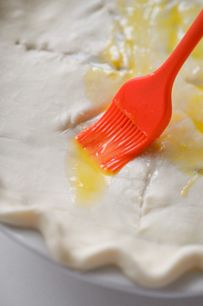 Brushing an egg wash over a pastry-topped pie.