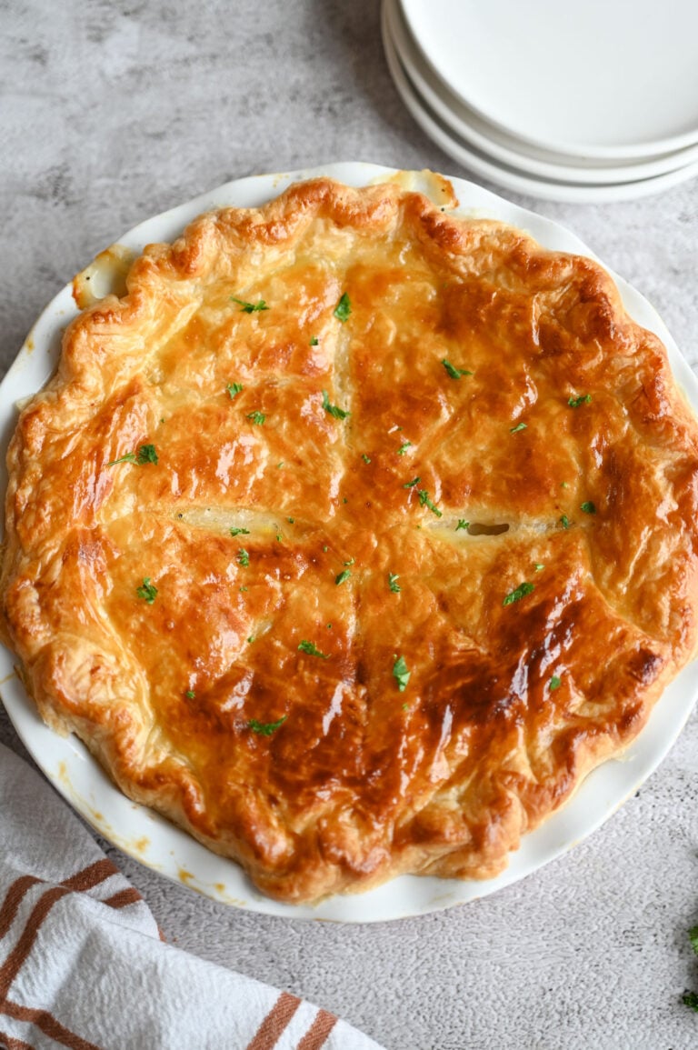 Puff Pastry Chicken Pot Pie with a shiny, flaky golden brown topping in a white ceramic pie plate.