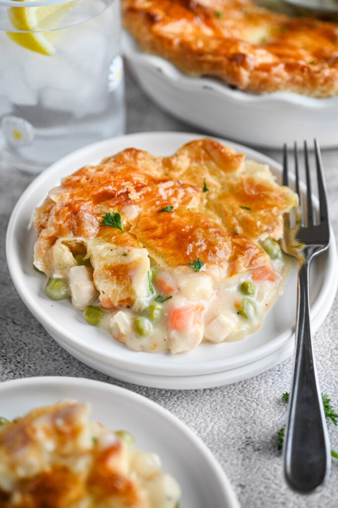 A spoonful of puff pastry chicken pot pie on a white plate with a silver fork next to it.